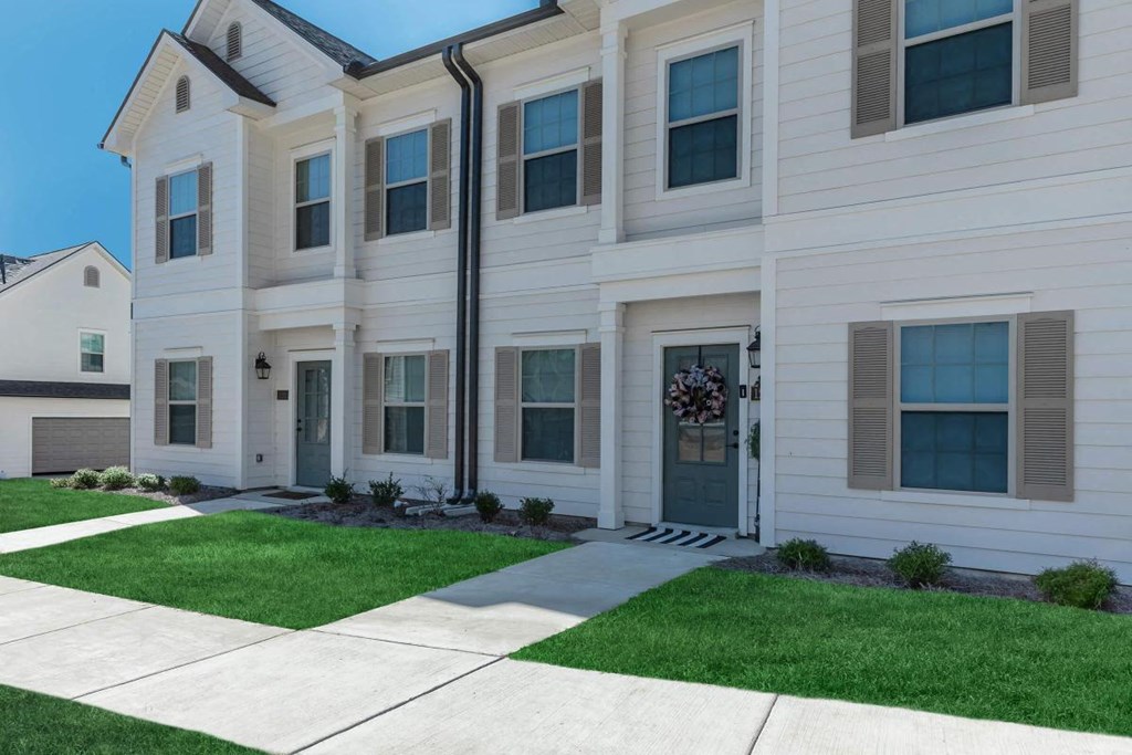 the front of a white house with a sidewalk and grass