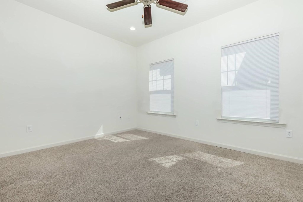 an empty living room with a ceiling fan and two windows