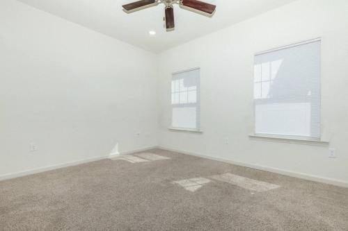 an empty living room with a ceiling fan and two windows