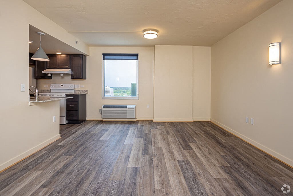 an empty living room with a kitchen and a window
