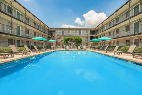 A large swimming pool in a resort with sun loungers and umbrellas. at The Cove at State Street Apartments, Baton Rouge, LA