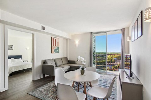 A living room with a white table and chairs, a couch, and a bed with a white headboard.