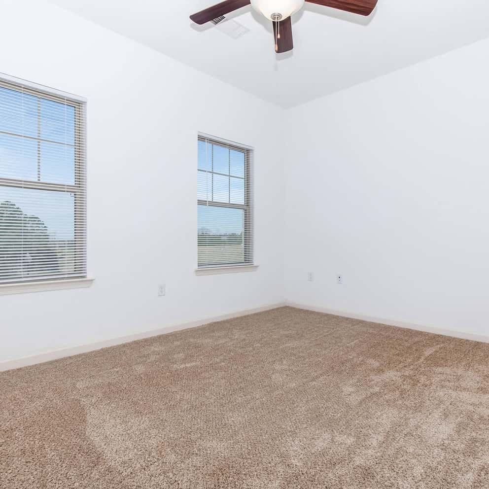 an empty room with two windows and a ceiling fan