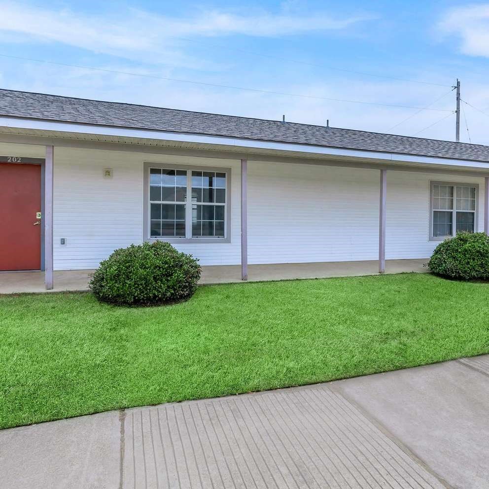 A small white house with a red door and a green lawn in front.