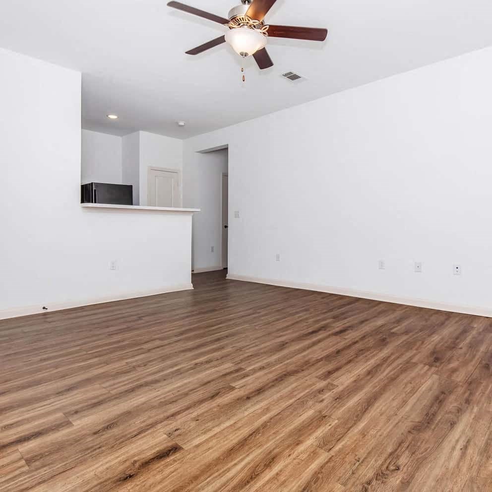 an empty living room with a ceiling fan and a kitchen