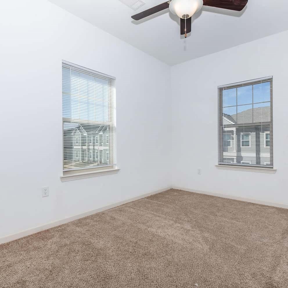 an empty room with a ceiling fan and two windows