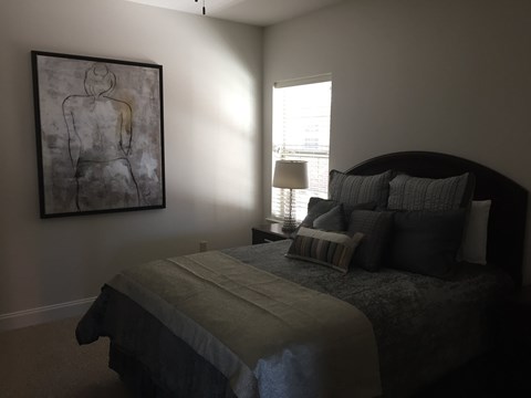 A bedroom with a bed, pillows, a lamp, and a painting on the wall.