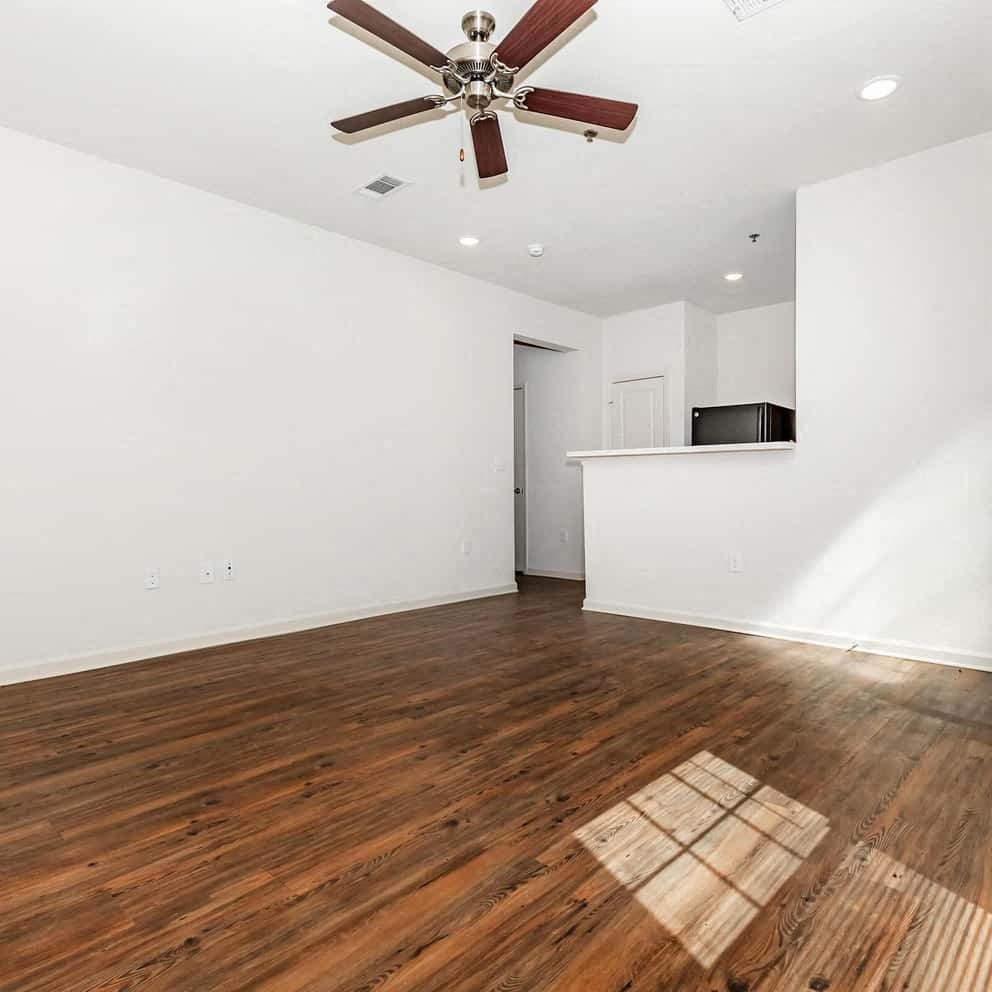 a room with hardwood floors and white walls with a ceiling fan