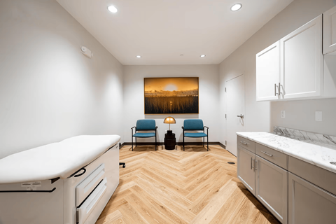 A modern kitchen with a wooden floor and a painting of a sunset on the wall.