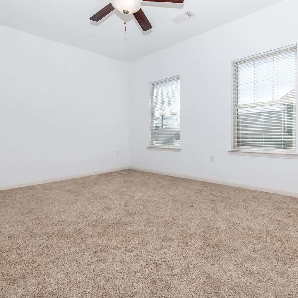 an empty room with a ceiling fan and two windows