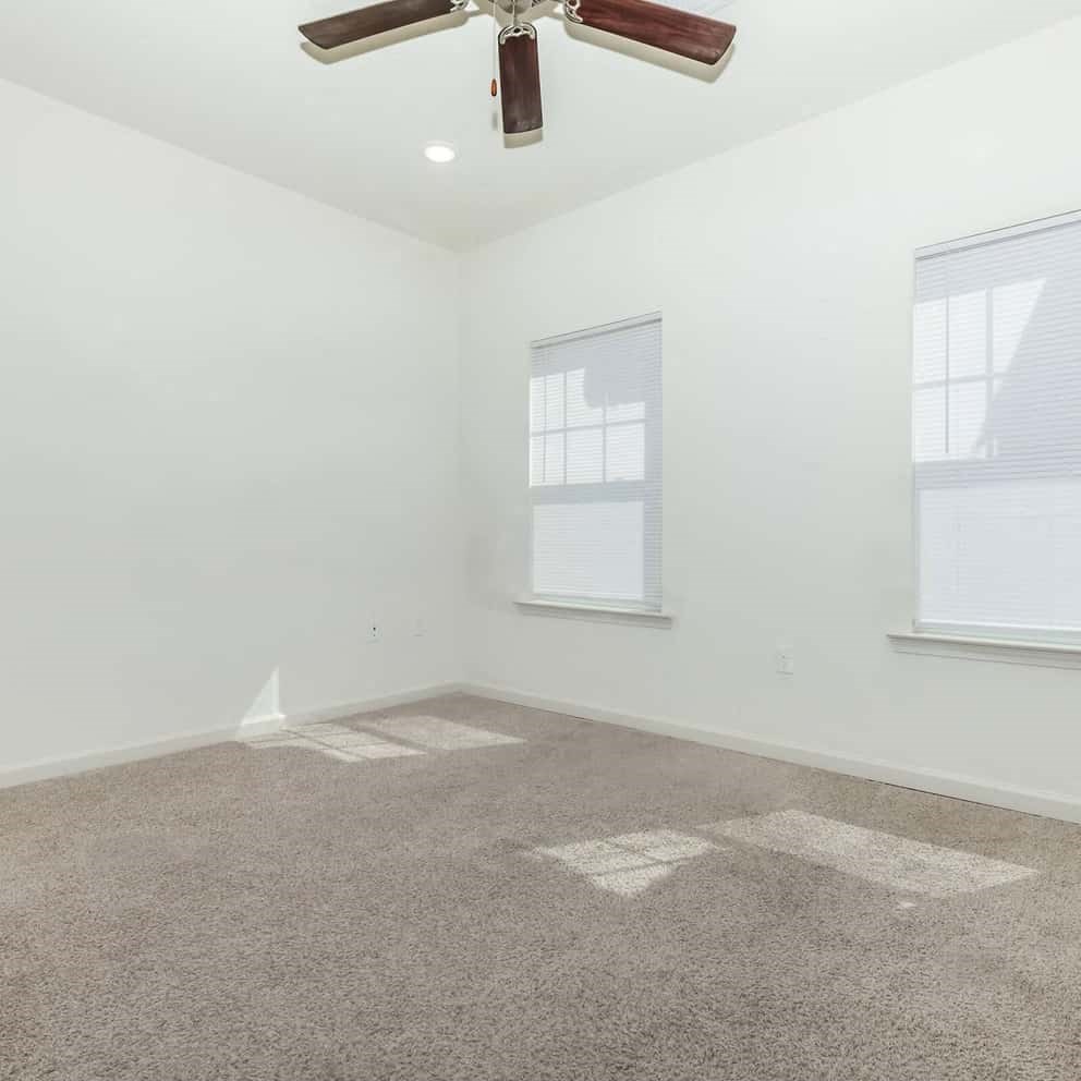 a bedroom with white walls a carpet and a ceiling fan