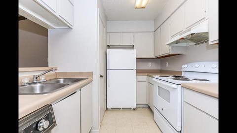 A white refrigerator is in the middle of a kitchen with white cabinets and a white stove.