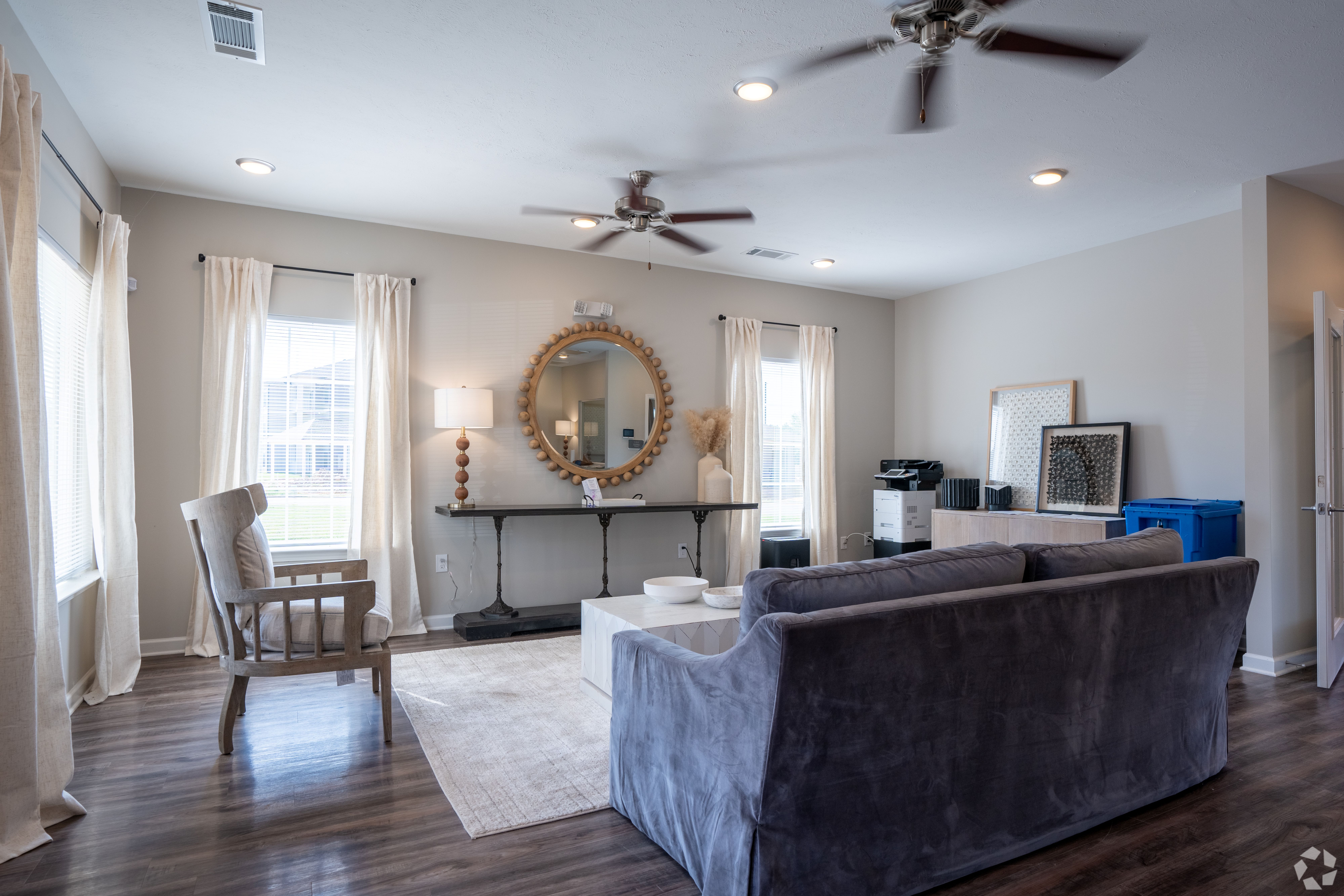 A living room with a grey couch, a chair, a mirror, and a ceiling fan.
