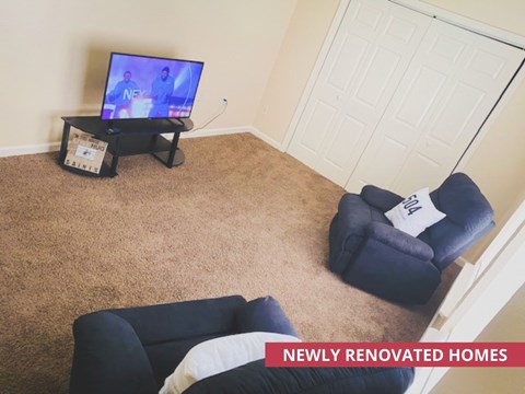 A living room with a TV on a stand and a blue chair with a white pillow.