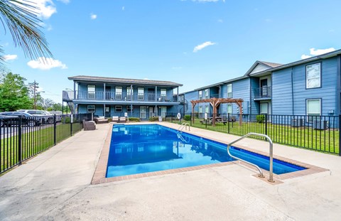 A swimming pool in front of a blue building with a black fence around it.