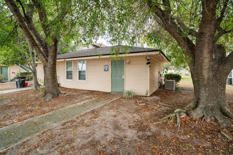 A beige house with a green door is surrounded by trees.