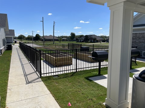 A black fence surrounds a grassy area with a white pillar on the right.