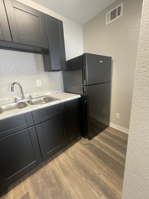 A black refrigerator in a kitchen with a white sink.