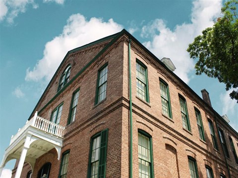 A red brick building with green windows and a white balcony.