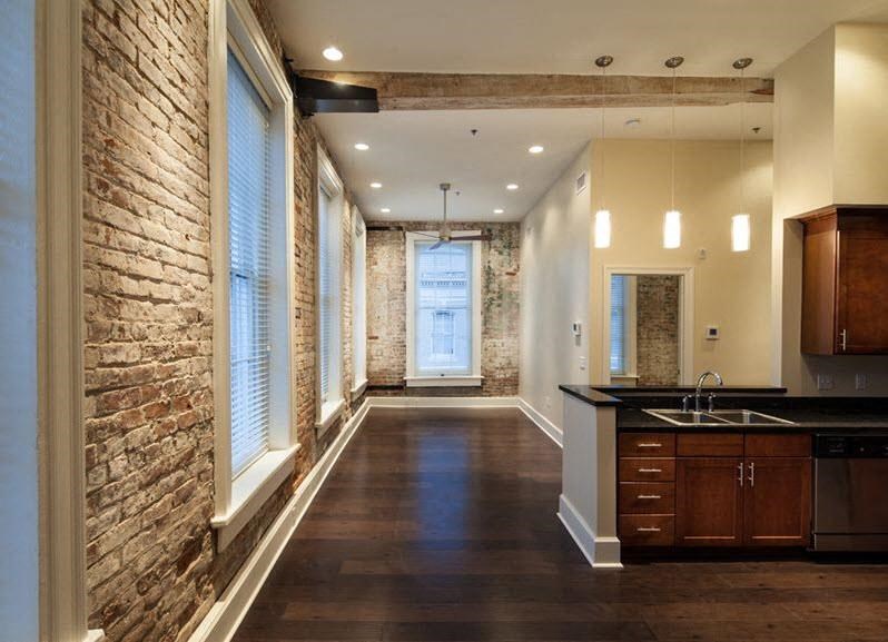 A long hallway with a brick wall on the left and a kitchen area on the right.