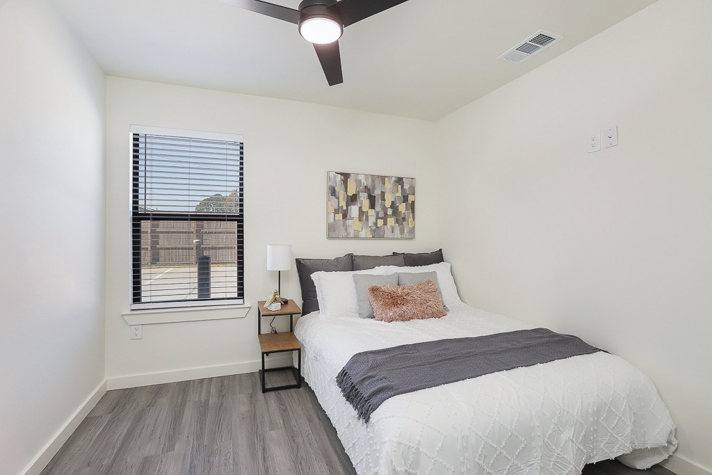 A bedroom with a bed, a ceiling fan, and a window with blinds.