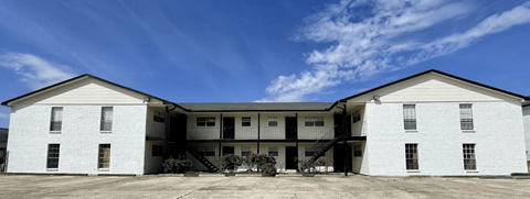 A white two-story building with a flat roof and a balcony on the second floor.