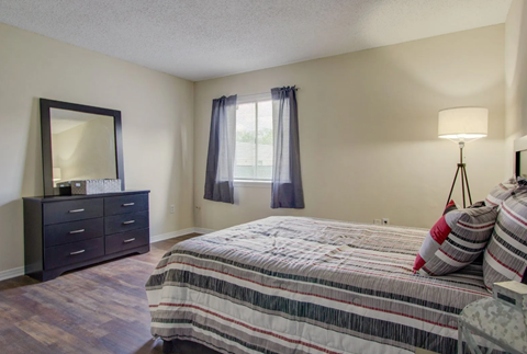 A bedroom with a bed, nightstand, and a dresser with a mirror.