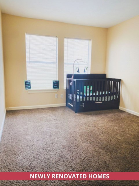 A baby crib sits in a corner of a room with a window.