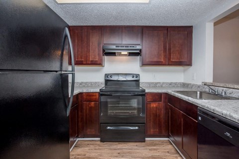 A black refrigerator is on the left in a kitchen with brown cabinets.