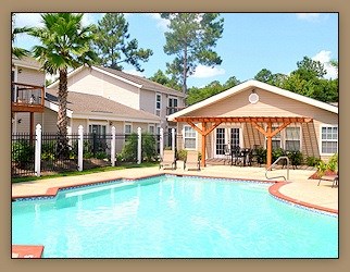 A pool in front of a house with a patio.