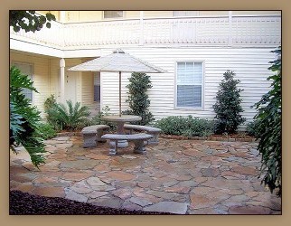A patio with a table and chairs is surrounded by plants.
