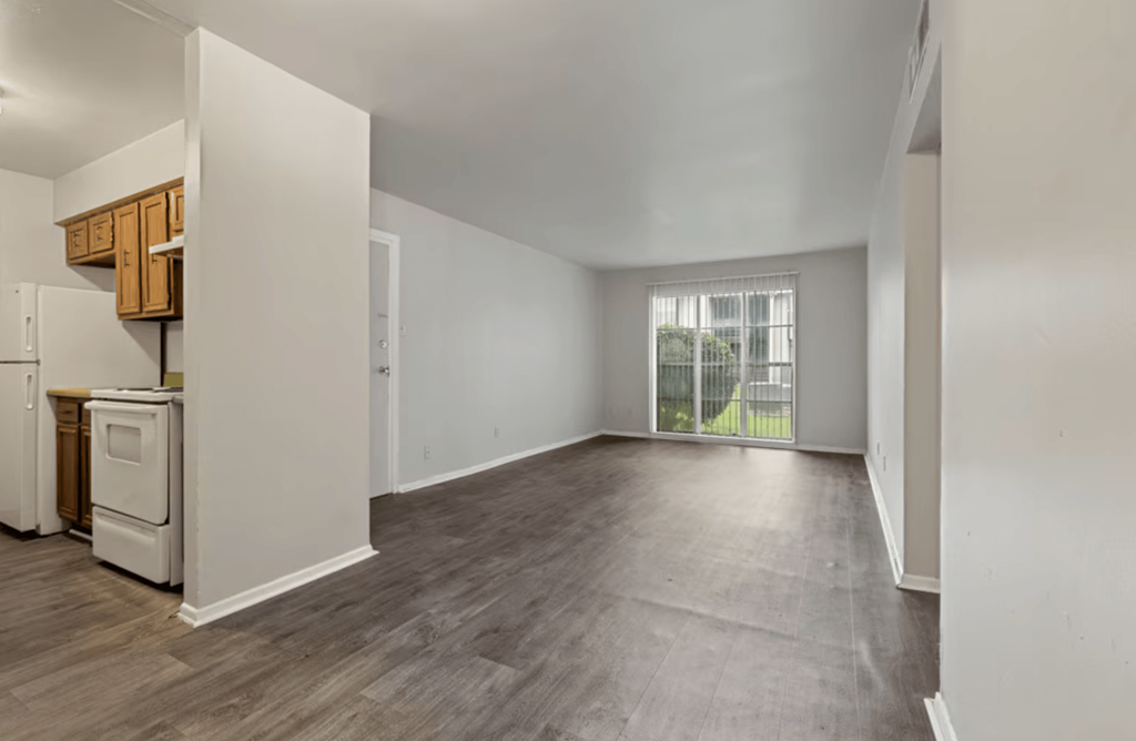 A spacious empty room with wooden flooring and white walls.