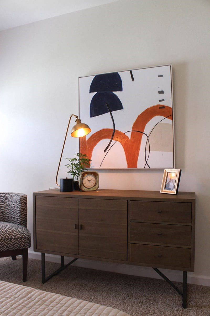 a dresser with a painting and a lamp on top of it