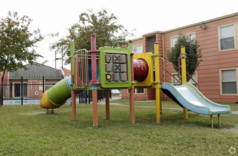A playground with a green and yellow slide, a red and green climbing structure, and a yellow and red swing set.