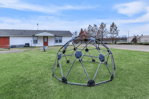 A large metal sculpture in the shape of a sphere is placed on a grassy field.