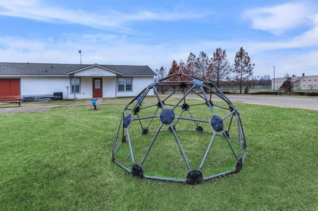 A large metal sculpture in the shape of a sphere is placed on a grassy area.