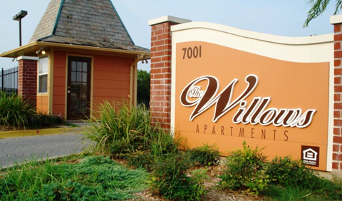 A small building is in front of a sign that says Willows Apartments.