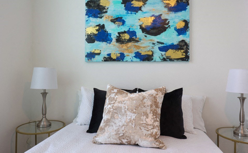 A bed with a white comforter and a painting above it.