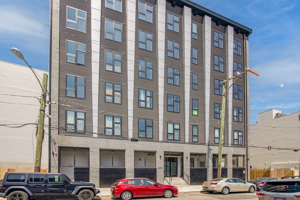 A tall building with a grey facade and a row of cars parked in front.