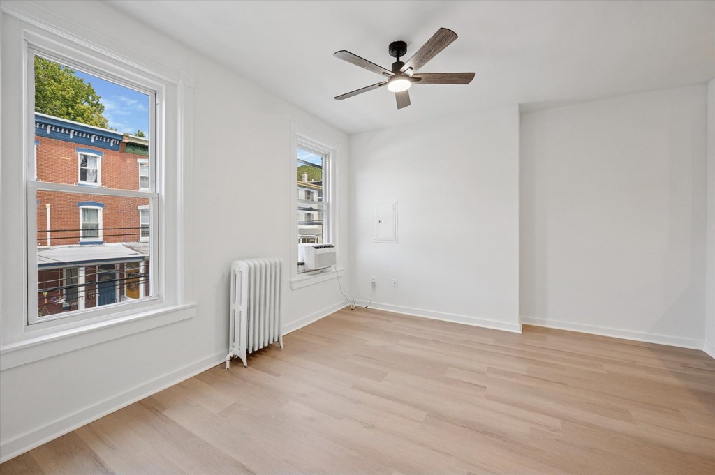 A room with a ceiling fan and a window overlooking a building.
