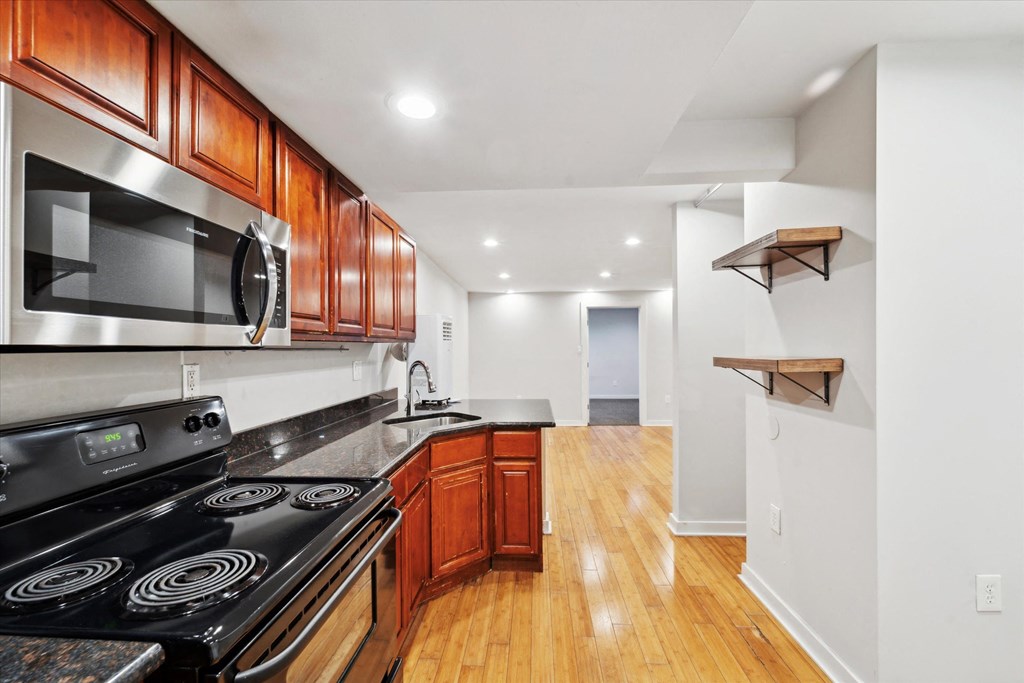 a kitchen with wood flooring and black appliances and wooden cabinets