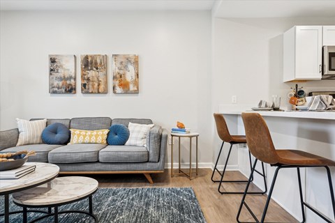 A grey couch with blue and yellow pillows sits in a living room with two chairs and a table.