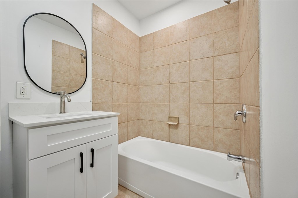 A bathroom with a white tub and beige tiles.