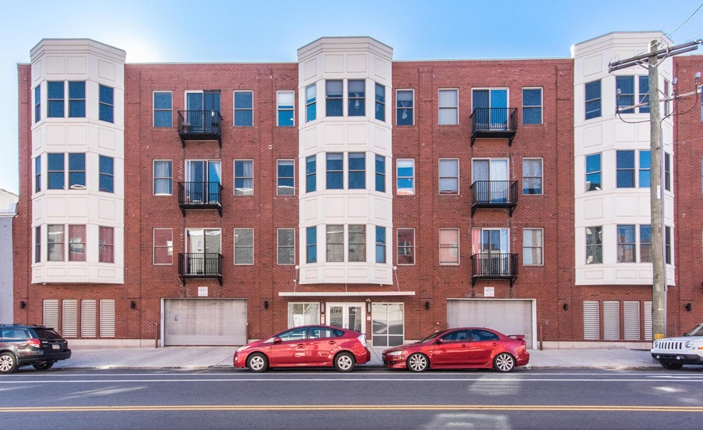a red brick apartment building with two red cars parked in front
