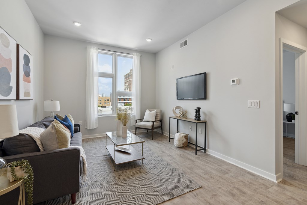 A living room with a grey couch, a white chair, a coffee table, and a flat screen TV mounted on the wall.