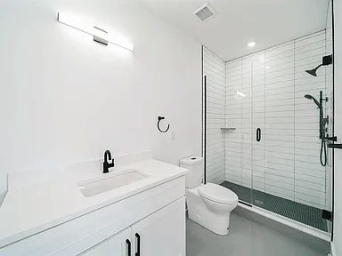 A white bathroom with a sink, toilet, and shower.