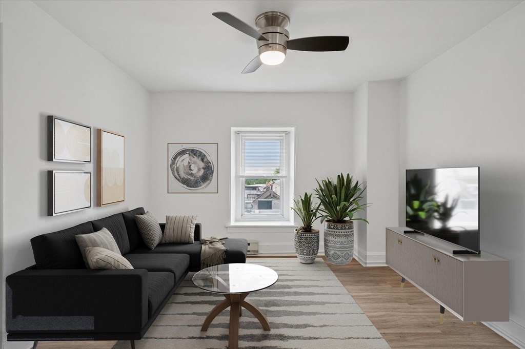 A living room with a black couch, a coffee table, a television, and a window with a view of the outside.