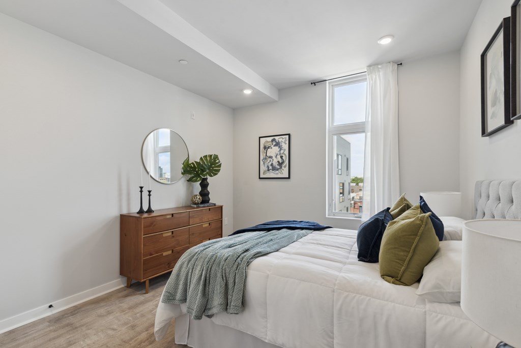 A bedroom with a white bed, a wooden dresser, and a mirror on the wall.