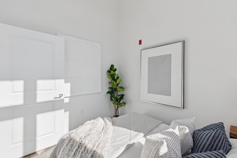 A bedroom with a bed covered in a white blanket and a framed picture on the wall.