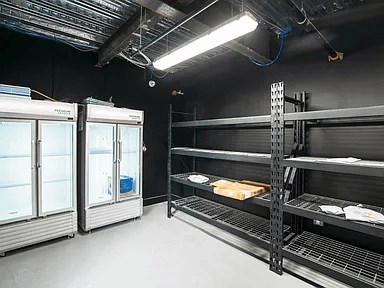 A storage room with shelves and two large refrigerators.